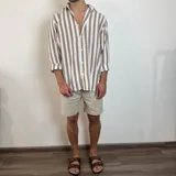 Camisa de lino a rayas verticales color beige y blanco, de corte holgado y manga larga con puños abotonados.