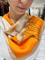 Pañuelo cuadrado de seda color naranja, blanco y beige, con estampado de hojas de ginkgo y líneas negras.
