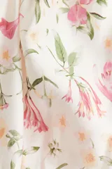 Blusa corta color blanco con estampado floral en tonos rosados y verdes. Presenta escote en V pronunciado, elásticos finos en la cintura y mangas globo cortas con elástico en los puños.