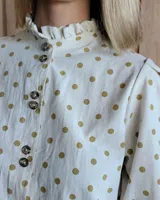 Camisa color beige claro con cuello con volados y mangas 3/4 abullonadas.