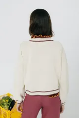 Cárdigan tejido en 50% algodón y 50% acrílico, color crema, con pespuntes tejidos en contraste color borgoña y bordado de limón en el pecho. Tiene cuello con volados, cierre frontal con botones y corte relajado.