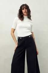 Pantalón de jean negro de corte ultra wide, tiro medio y detalles metálicos en la cintura.