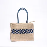 Bolso tipo tote de yute color beige con diseño geométrico azul y asas de soga azul.