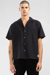 Camisa negra de manga corta con cuello camp y calce relajado. Confeccionada en mezcla de algodón y lino con botones de coco con logo y parche característico de Polonio.