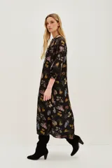 Vestido midi negro con estampado floral en tonos pastel y amarillos. Presenta escote pronunciado en V, mangas largas con puños anchos y detalles de bordado o pasamanería oscura en los bordes.