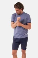 Remera de manga corta color azul grisáceo con cuello mao y tapeta de botones. Los puños de las mangas y el cuello son de color azul marino contrastante. Presenta un pequeño logo bordado en el pecho.