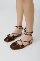 Sandalias chatitas de cuero color bordó, con puntera cuadrada y tiras finas que se atan al tobillo.