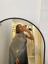 Vestido largo de tafeta con brillo, color gris o plateado, con escote asimétrico de un solo hombro y una pieza de seda liviana que cae como una capa o chal.