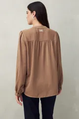 Camisa color marrón claro con cuello mao, mangas 3/4 abullonadas y cierre frontal con botones. Presenta pequeños pliegues en los hombros y detalle calado sutil.