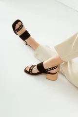 Sandalias de tacón de madera con tiras de gamuza marrón y detalles de tachas metálicas.