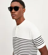 Polo de hombre con corte comfort, confeccionada en tejido de punto de algodón a rayas horizontales blancas y negras. Tiene cuello inglés con botones y mangas cortas.