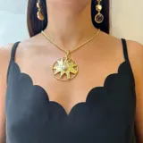 Collar con cadena dorada y dije colgante de sol con textura rugosa y una perla redonda engarzada en el centro.