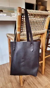 Bolso tote de cuero color marrón oscuro con doble asa larga de cuero y remaches metálicos.
