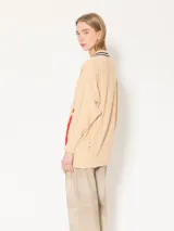 Sweater beige de punto con cuello en V con rayas azul marino y tiras trenzadas rojas y rosas en los laterales.