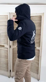 Campera negra con capucha, cierre frontal y bolsillos laterales con cierre. Presenta un logo bordado en el pecho y un parche con diseño de paisaje en la manga.