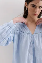 Camisa celeste de algodón con bordado calado, cuello en V y mangas largas abullonadas con puños elásticos.