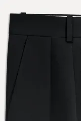 Pantalón negro de tiro medio con cintura con trabillas, bolsillos laterales y con solapa en espalda. Detalle de pinzas y raya planchada en delantero. Cierre frontal con cremallera, botón y ganchos metálicos.