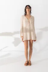 Vestido corto color crema, tejido con detalle de costuras en color ladrillo en ruedo y mangas. Escote en V con lazos ajustables y mangas largas oxford con aberturas y lazos.