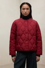 Campera acolchada de color bordó con diseño de costuras onduladas tipo 'onion'. Presenta cuello redondo, cierre frontal con botones a presión y bolsillos laterales. Confeccionada en poliéster reciclado con acabado repelente al agua.