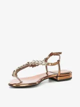 Sandalia color bronce con tira en el dedo y diseño entrelazado con apliques de strass. Cuenta con pulsera ajustable en el talón y una base plana de leve altura.