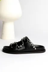 Sandalias negras de cuero con dos tiras gruesas con hebillas plateadas y apliques de esferas metálicas.