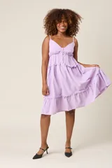 Vestido corto lila con breteles finos, escote en V con botones y falda escalonada con volados.