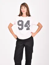 Remera de manga corta color rosa pálido con cuello redondo y un gran estampado frontal de los números "94" y una estrella en gris oscuro con efecto desgastado.