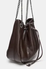 Bolso tipo saca de cuero sintético marrón oscuro, con fruncido superior ajustable mediante cordón. Posee asa de hombro con detalle de cadena metálica oscura y bolsillo interior con cierre.
