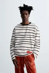 Camiseta relaxed fit de manga larga confeccionada en tejido compacto de algodón a rayas horizontales blancas y negras. Tiene cuello redondo y detalle de estampado de flores rojas en el bajo. Edición especial Zara x Otis Kwame Kye Quaicoe.