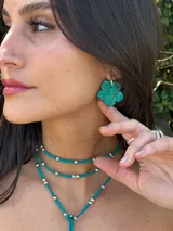Aros colgantes con forma de trébol de cuatro hojas color verde esmeralda con textura brillante.
