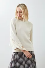 Sweater beige claro de tejido de punto con cuello redondo y mangas largas con flecos.