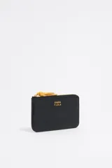 Monedero negro de cuero con cierre de cremallera y tirador de cordón amarillo. Incluye bolsillo interior y placa metálica con el logo de la marca.