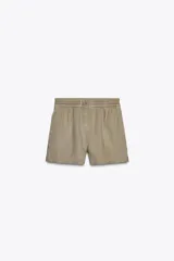 Shorts color beige de tiro medio confeccionados en lino 100%. Presentan bolsillos laterales ocultos en costura y de parche en la espalda. La cintura es elástica y el bajo tiene aberturas laterales. El cierre frontal es con botones.