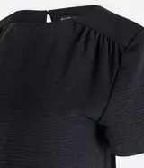 Blusa negra de poliéster con cuello redondo, manga corta y detalle de pliegues en los hombros. Cierre con botón en la espalda.