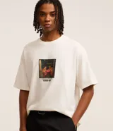 Remera de corte boxy color crudo, con cuello redondo y mangas cortas. Estampa frontal con dibujo de perros jugando a las cartas y texto 'underappreciated crew 1989-90'.