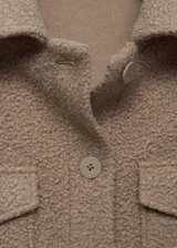Chaqueta color gris topo de tejido bouclé, con cuello camisero, cierre frontal con botones, dos bolsillos de parche con solapa y botón en el pecho, y mangas largas.