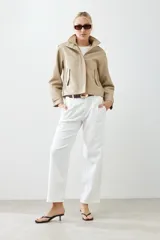 Chaqueta corta color beige de cuero sintético, con cuello alto, cierre frontal con botones a presión y bolsillos laterales con solapa.
