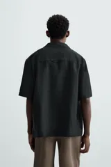 Camisa color marrón oscuro de corte relaxed fit, confeccionada en tejido de lino. Tiene cuello bowling, manga corta, bajo con aberturas laterales y cierre frontal de botonadura.