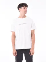 Remera blanca de corte recto con estampa fotográfica de edificios en la parte frontal.