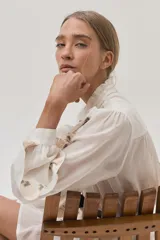 Blusa blanca de viscosa con cuello mao, cierre frontal con botones, mangas largas abullonadas con volados y bordados florales.