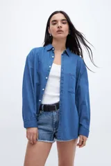 Camisa de denim azul de algodón, con cuello solapa, calce relaxed, manga larga y bolsillo cuadrado en el pecho. Cierre frontal con botones personalizados.
