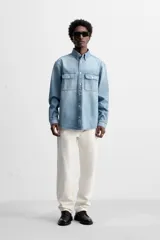 Camisa celeste de denim de algodón, corte relaxed fit, con cuello solapa, manga larga con puños abotonados, dos bolsillos de parche con solapa en el pecho, efecto lavado y cierre frontal abotonado.