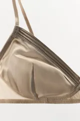 Bralette triangular color champagne de tejido satinado con detalle de plisado. Tiene tirantes finos ajustables y cierre trasero con ganchos metálicos.