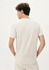 Camiseta beige de manga corta con estampa de hojas en el bolsillo.