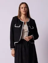Chaqueta de tweed blanca con ribete negro, escote a la base, abertura central con botones, bolsillos delanteros y puños con aplique de botones perlados.