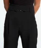 Pantalón negro de corte carrot, con trabillas en la cintura, detalle metálico y pliegues.