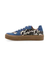 Zapatillas bajas con estampado de vaca en blanco y negro, detalles en gamuza azul y suela marrón.