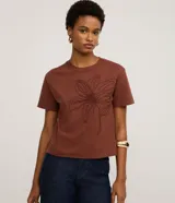 Remera de manga corta color marrón, con cuello redondo y corte recto. Presenta un bordado grande en relieve de una flor en el centro del pecho.