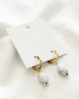 Aros Valente dorados con colgante de piedra blanca veteada en gris y detalle de bolita dorada. El aro es de acero.