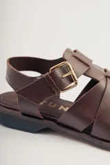 Sandalias bajas de cuero marrón con tiras entrecruzadas y hebilla dorada.